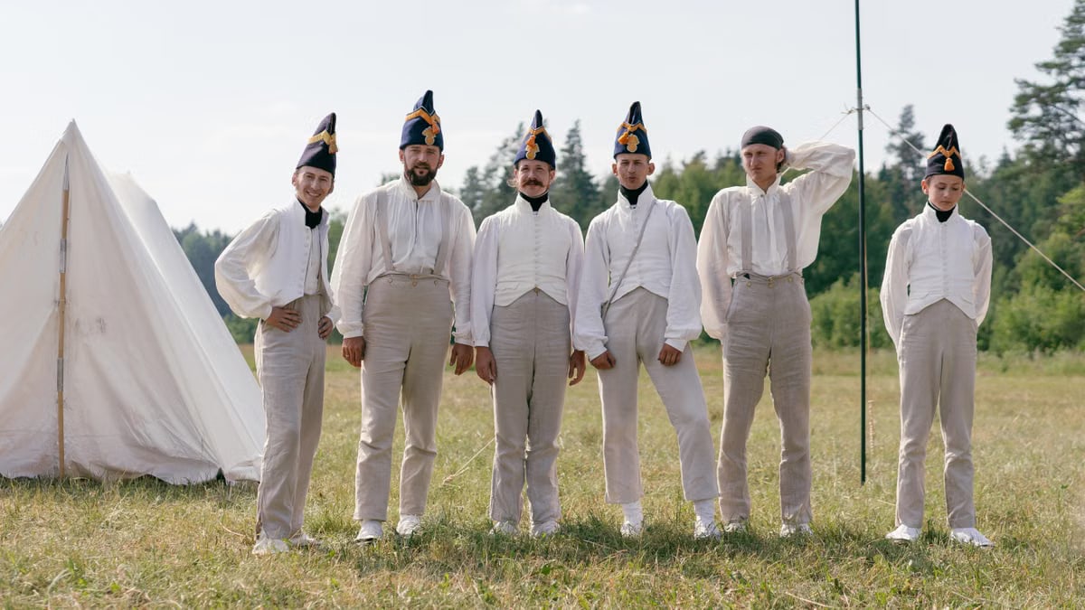 A group of soldiers in historical uniforms standing in a field beside a tent.
